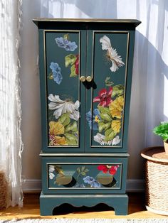 an armoire with flowers painted on it next to a potted plant and wicker basket