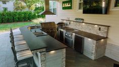 an outdoor kitchen with stainless steel appliances and bar stools on the outside patio area