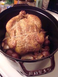 a cooked chicken in a skillet on top of a stove with potatoes and onions