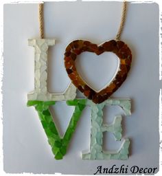 the word love spelled with sea glass and a heart hanging from a string on a white background