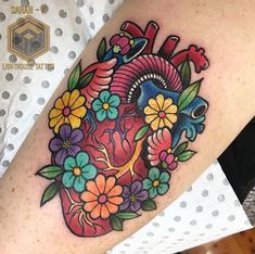 a heart tattoo on the arm with flowers and leaves around it, which is also in color