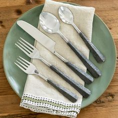 a green plate topped with forks and spoons next to a napkin on top of a wooden table