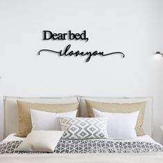 a bed with white sheets and pillows under a black sign that says dear bed, i love you