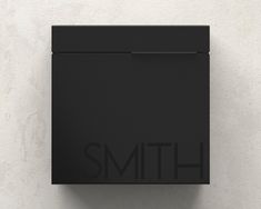 a black square sign mounted to the side of a white wall that says smith on it