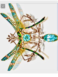 a dragonfly brooch sitting on top of a white table next to a blue diamond