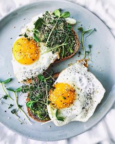 two fried eggs on toast with greens and sprouts are served on a plate