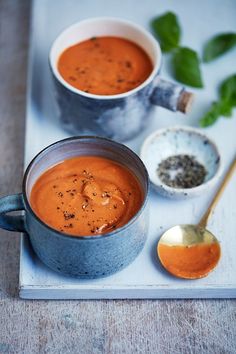 two bowls of tomato soup on a tray with spoons and pepper shakers next to them