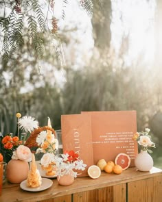 a table topped with oranges and flowers on top of a wooden table next to a sign