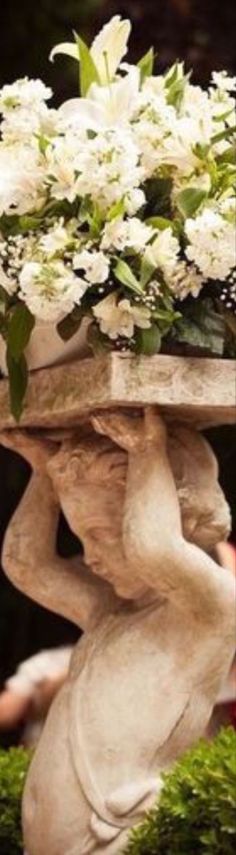 a white flower arrangement on top of a stone pedestal in a garden with green grass