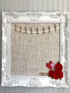 a white frame with red flowers and clothes pins attached to the side, hanging on a wall