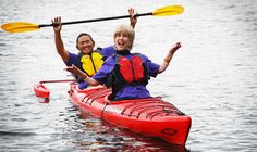 two people in a kayak on the water with their arms up and one person smiling