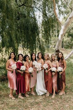 a group of women standing next to each other in front of a lush green tree