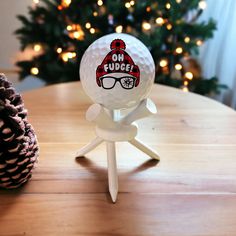 a white golf ball with a red hat and glasses on it sitting on a table next to a pine cone