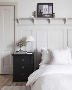 a bedroom with white bedding and pillows on the headboard, next to a night stand