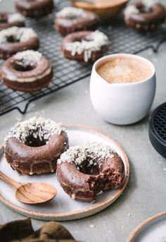 two chocolate doughnuts on a plate next to a cup of coffee and spoon