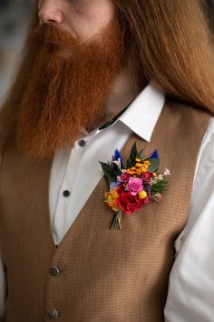 a man with long red hair wearing a brown vest and flower boutonniere