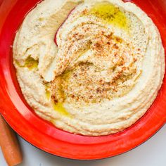 a red plate topped with hummus next to a carrot and an orange bowl filled with dip