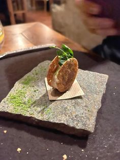 a small piece of food sitting on top of a stone slab next to a glass of wine