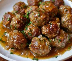 meatballs covered in gravy and garnished with parsley on a white plate