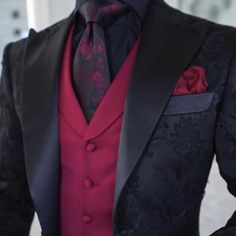 a man in a black suit and red shirt is wearing a flowered boutonniere