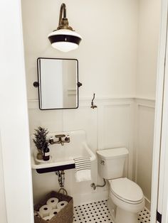 a white toilet sitting next to a sink in a bathroom under a mirror and light