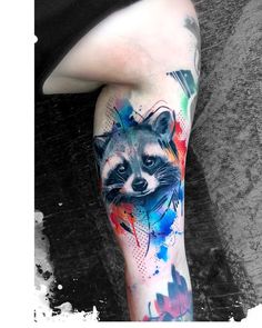 a raccoon tattoo on the leg of a person with colorful paint splatters