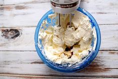 a food processor with whipped cream in it on top of a white wooden table next to a blue bowl