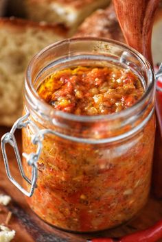 a glass jar filled with food sitting on top of a wooden table next to bread