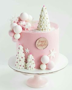 a pink christmas cake with white decorations and trees on the top is sitting on a plate