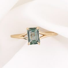 a ring with an emerald colored stone on it sitting on a white cloth covered surface