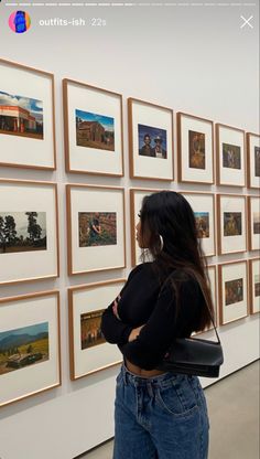 a woman standing in front of a wall with pictures on it and looking at them