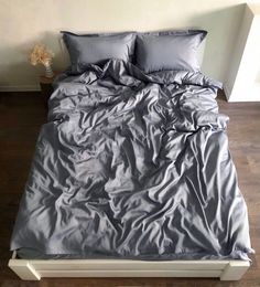 an unmade bed with grey sheets and pillows