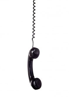 an old - fashioned black telephone is hanging from a metal hook on a white background