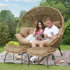 a man and woman are sitting in a chair on a blanket outside with an open book