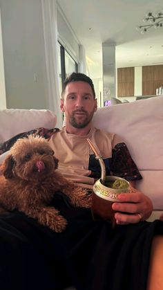 a man sitting on a couch holding a cup and a dog