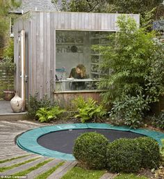 a garden with a small shed in the background and a person sitting at a window