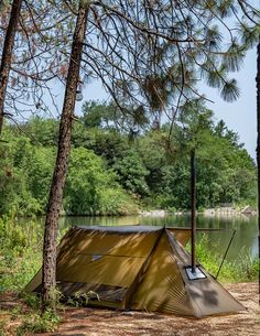 a tent pitched up in the woods next to a lake with trees and water behind it