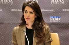 a woman sitting at a table with a microphone in front of her and a media panel behind her