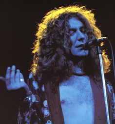 a man with long hair and no shirt on holding a microphone in front of him