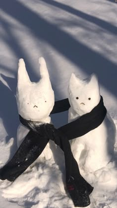 two snowmen with black scarves on their heads and scarfs wrapped around them in the snow