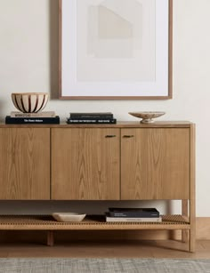 a wooden sideboard with books on it in front of a framed art piece and rug