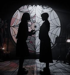 two people standing next to each other in front of a large circular window at night