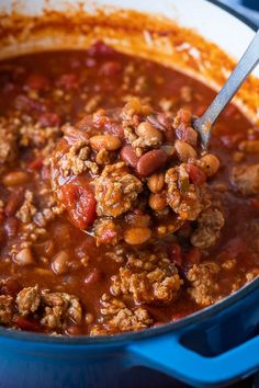 a spoon full of chili and beans in a blue pot