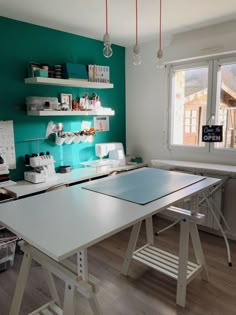 a room with green walls and white tables in the center, along with shelves filled with sewing supplies