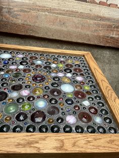 a close up of a wooden table with many different colored glass items on it and a brick wall in the background