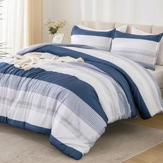 a bed with blue and white comforters in a room next to a plant on the floor