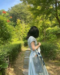 a woman in a blue dress walking down a path with a bag on her shoulder