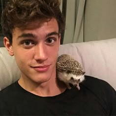 a young man is holding a hedgehog on his shoulder