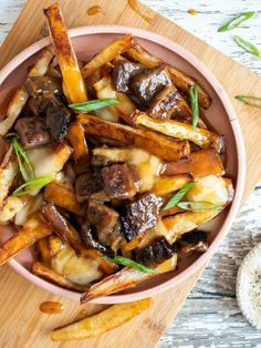 a pink bowl filled with french fries covered in mushrooms and sauce on top of a wooden cutting board