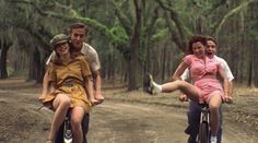 three people riding bikes down a dirt road